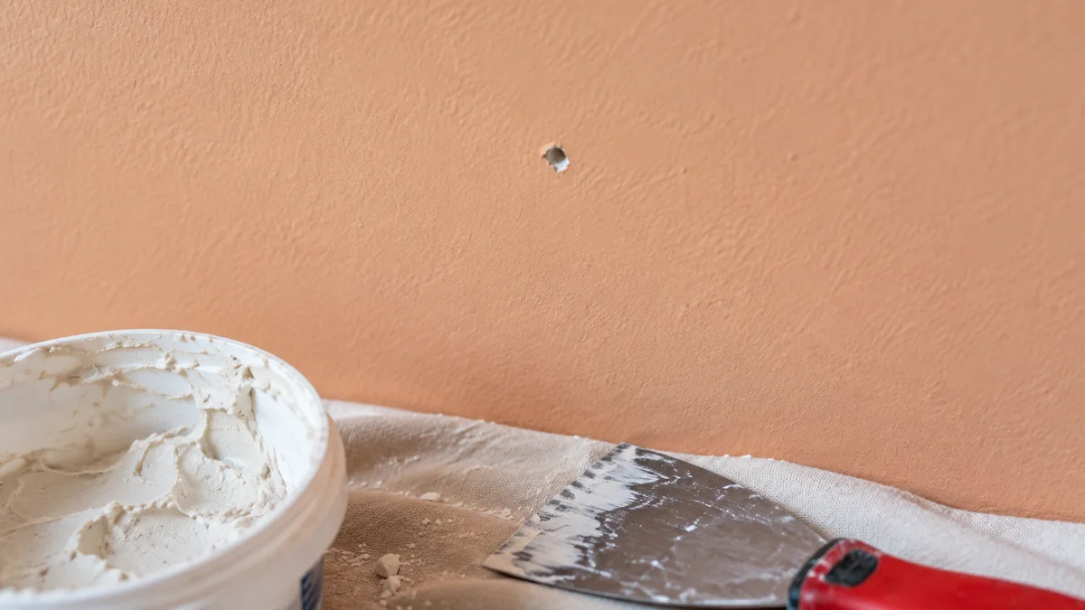 Small nail hole in peach-colored drywall beside patching tools